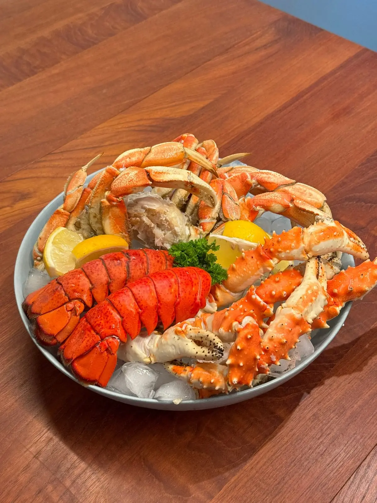 A platter of crab legs and cooked lobster tails on ice with lemon