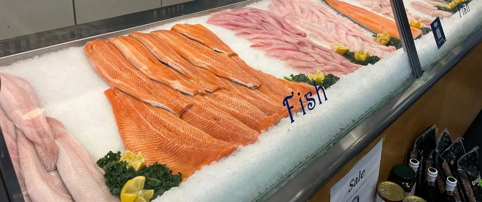 Fresh salmon and white fish fillets laid out on ice along the fish counter