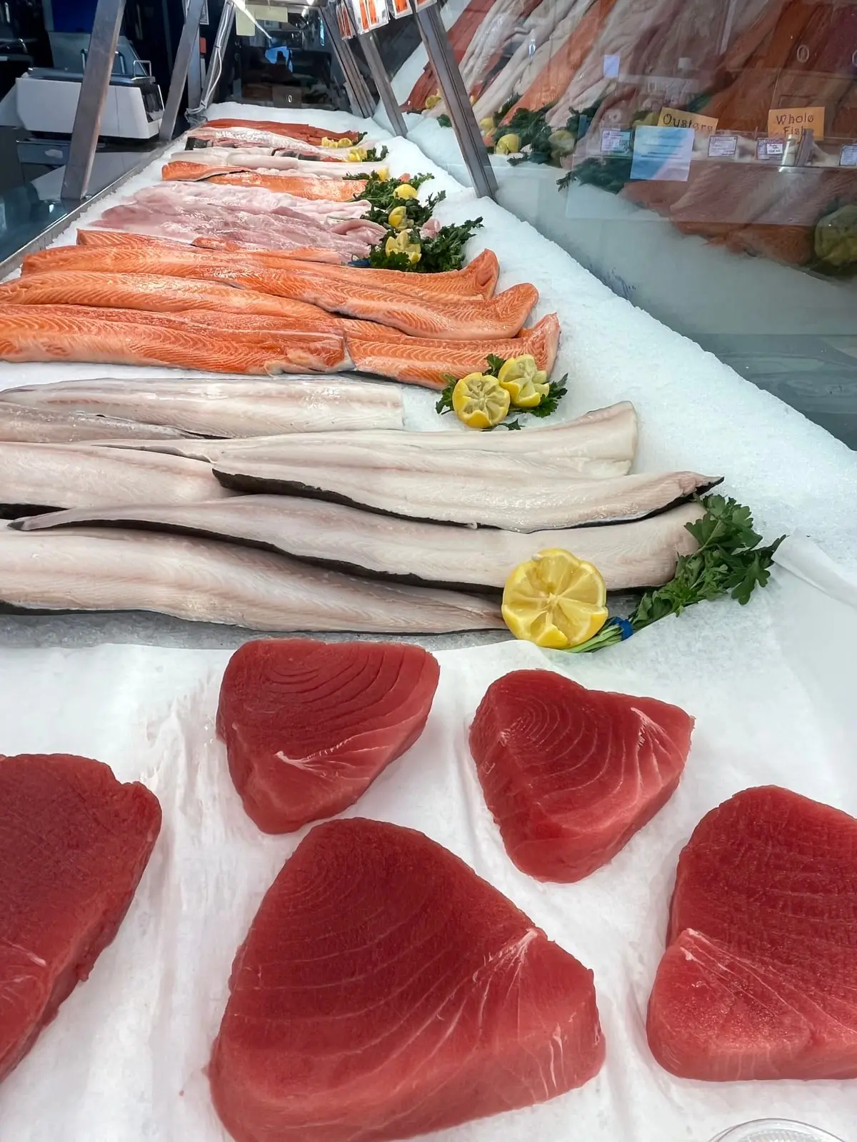 Tuna steaks, white fish and salmon fillets arranged on ice with lemon and kale