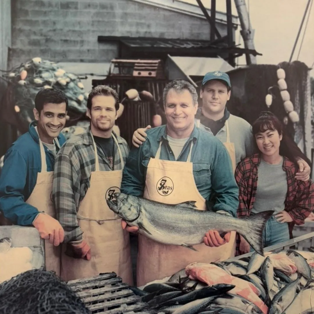 Archive photo from an old bank advertisement: Big John holding a king salmon on the docks, flanked by his sons and two actors