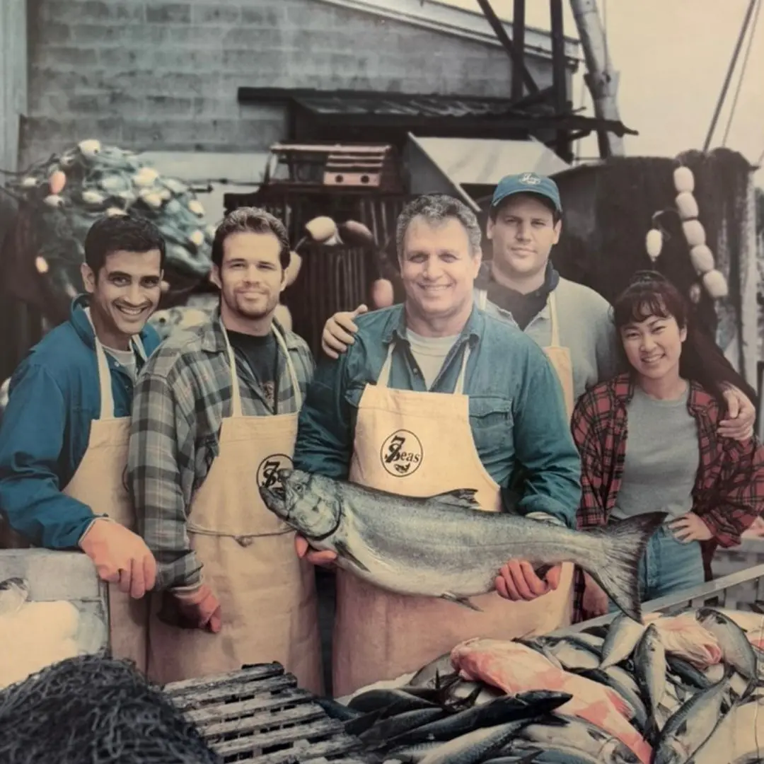 Archive photo from an old bank advertisement: Big John holding a king salmon on the docks, flanked by his sons and two actors