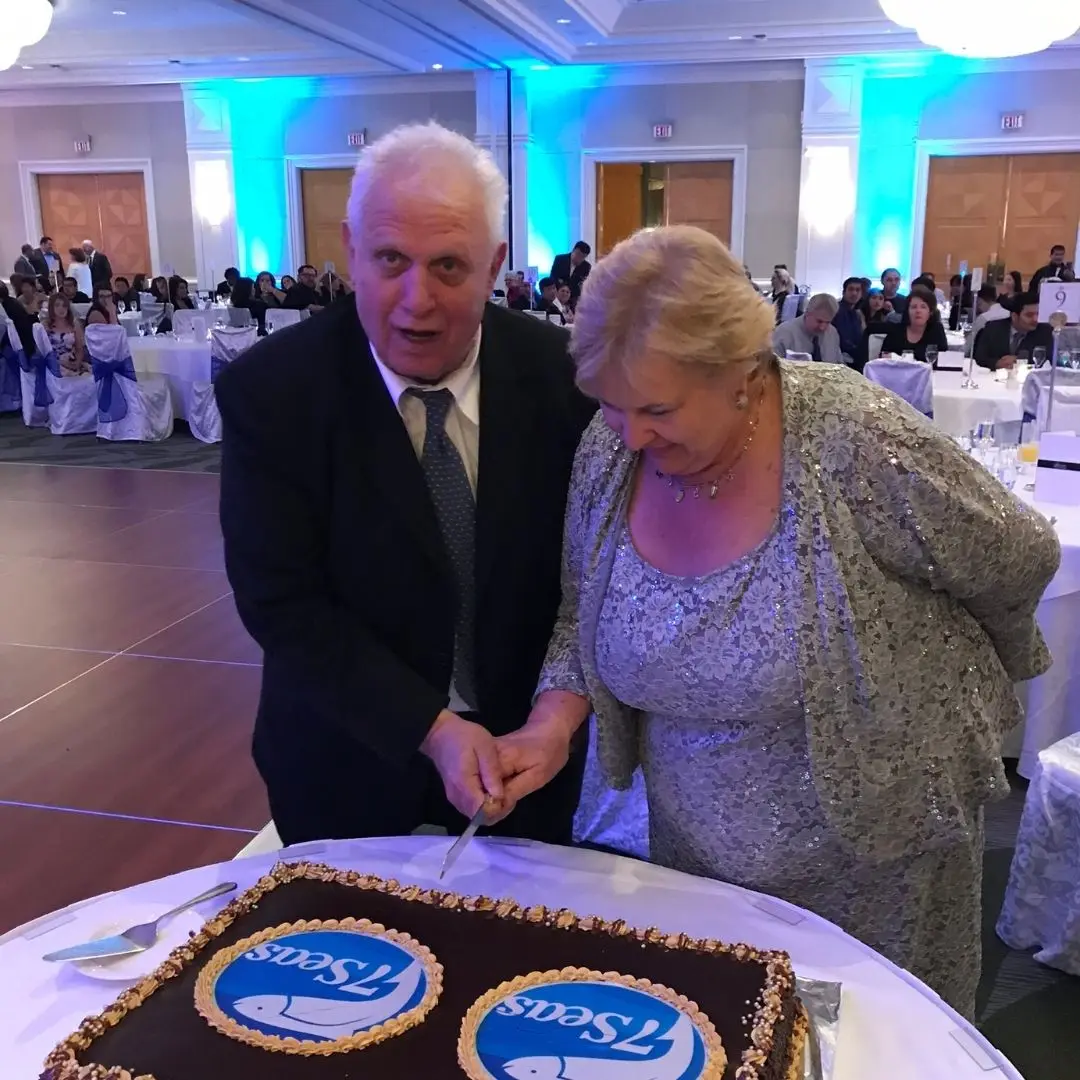 John and Debbie cutting a chocolate cake decorated with 7 Seas logos at the annual company Christmas party