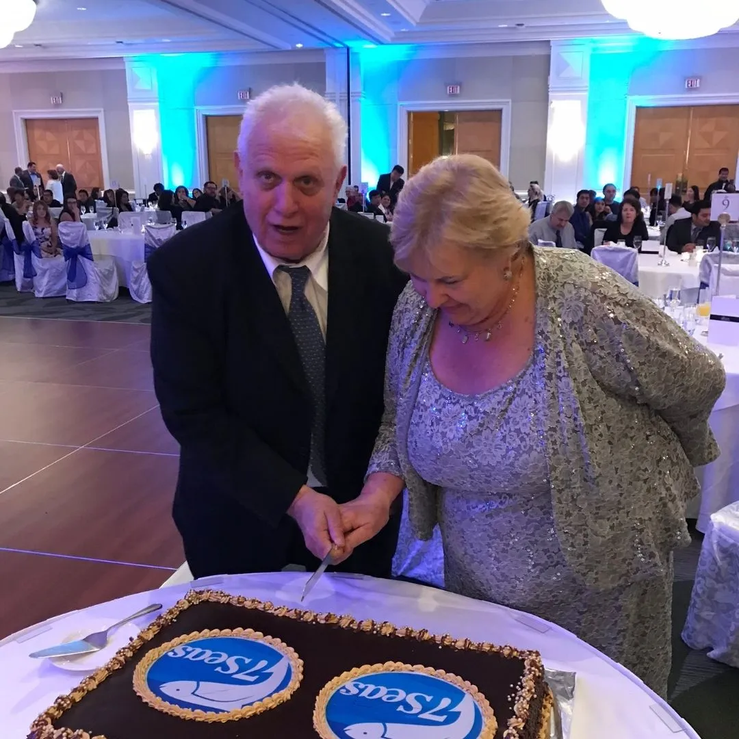 John and Debbie cutting a chocolate cake decorated with 7 Seas logos at the annual company Christmas party