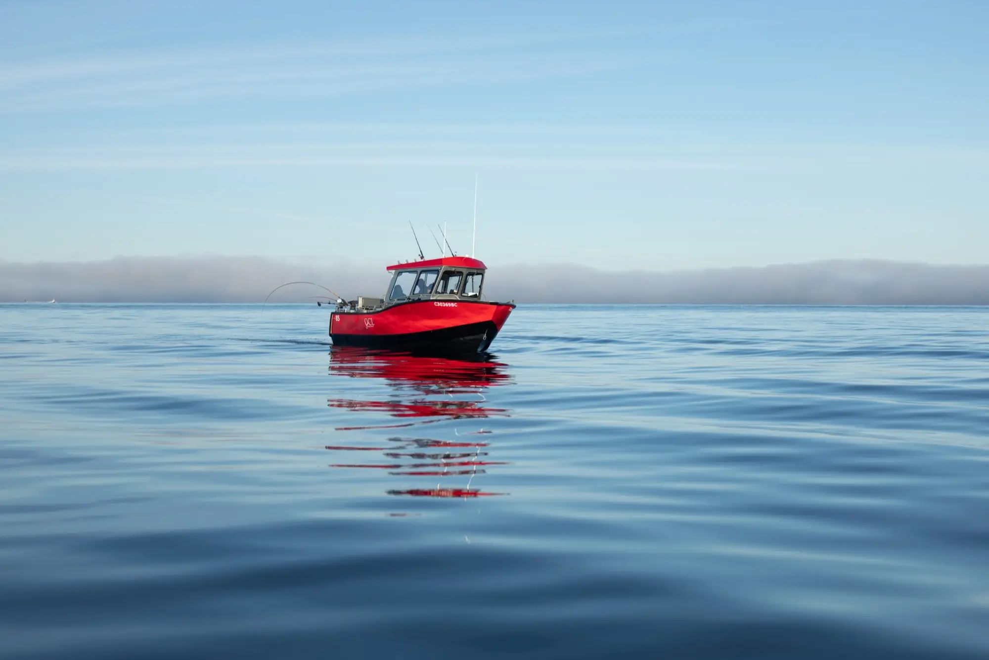 A red aluminum boat sitting on glassy BC coastal water under a clear sky