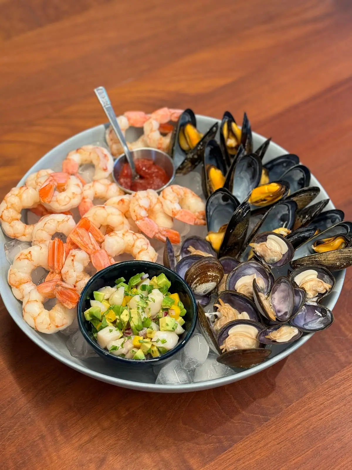 A chilled seafood platter of cooked prawns, mussels and clams on ice with cocktail sauce
