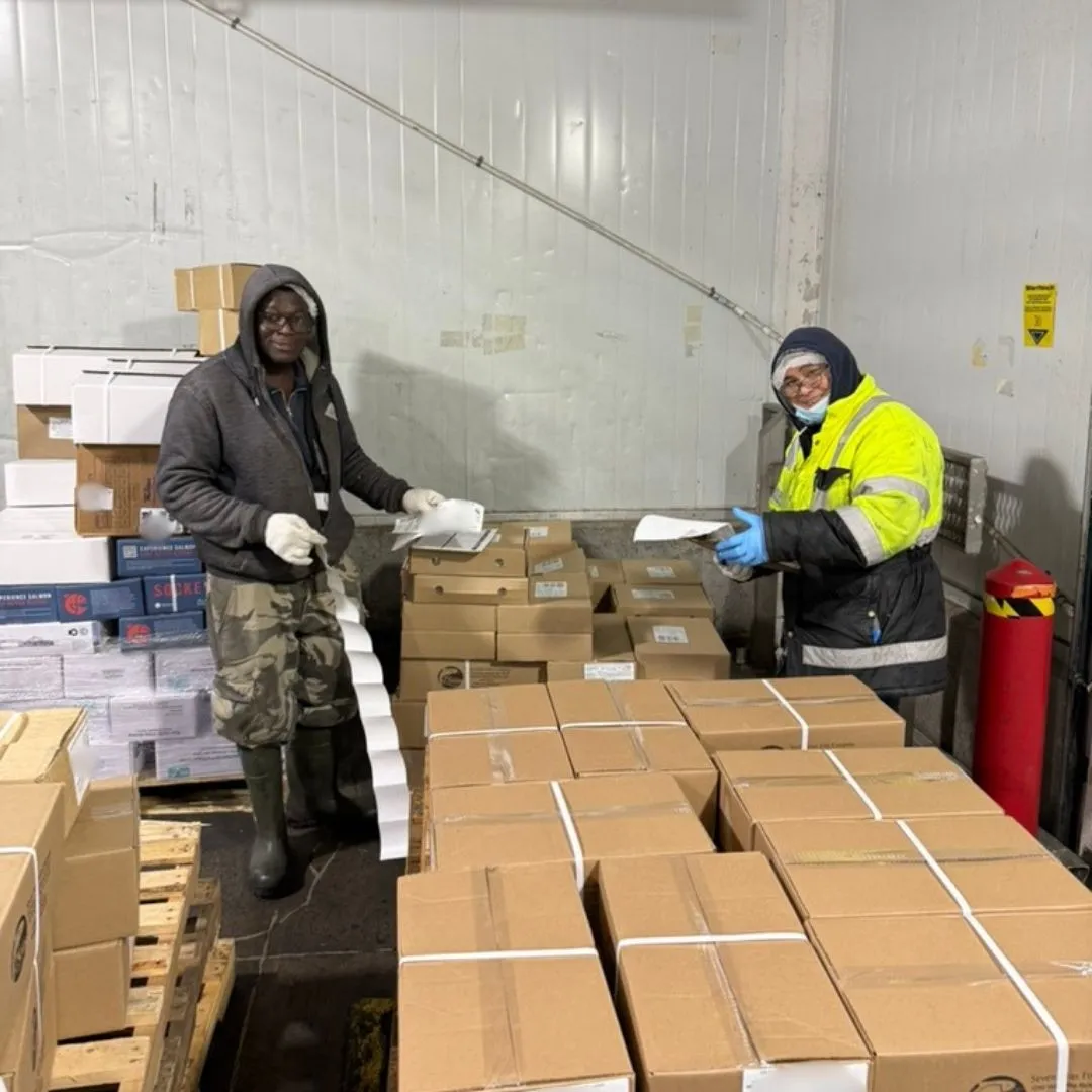 Two team members labelling boxed product on pallets before shipping