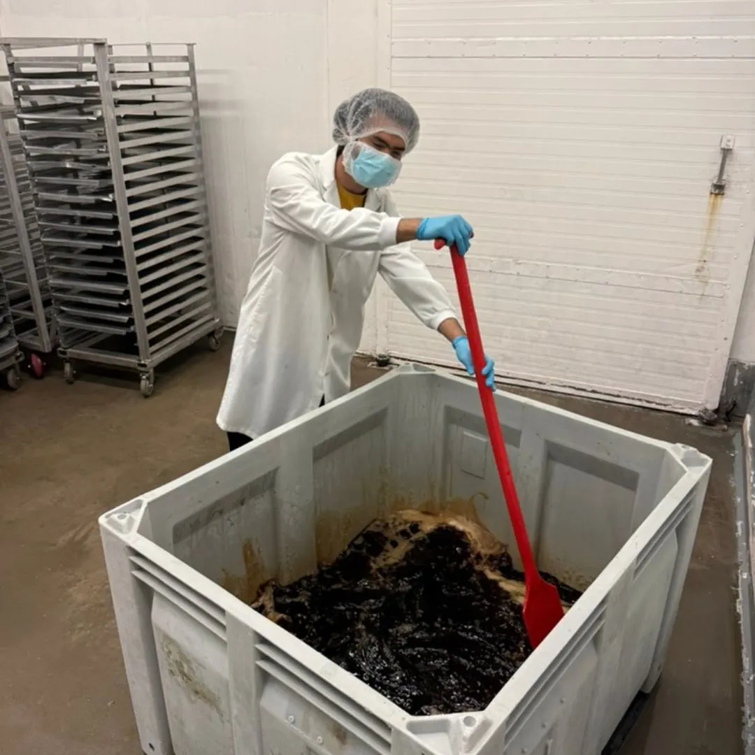 Team member stirring a large tote of pre-smoke marinade for salmon candy
